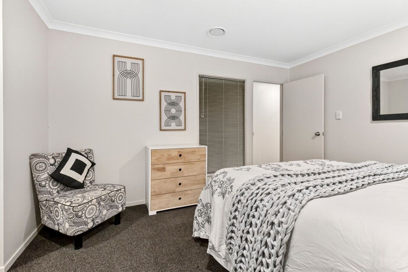 A bedroom with a bed, a dresser, a chair, and two wall art pieces.