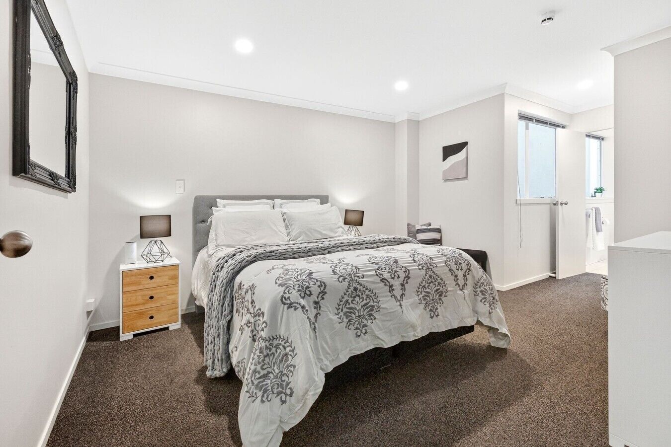 A bedroom with a bed, bedside tables, a dresser, a window, and a door.
