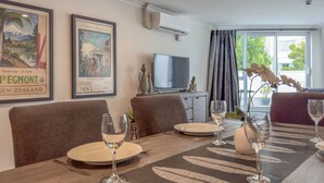 Un coin repas avec une table dressée pour quatre personnes, un téléviseur posé sur un meuble et des affiches de voyage encadrées accrochées au mur.