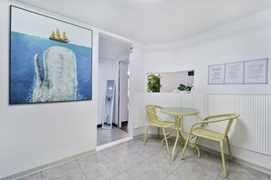 Una habitación con un cuadro grande de una ballena, una mesa con sillas, un radiador y una puerta que da a otra estancia.