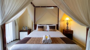 A hotel room with a bed, curtains, a nightstand, a lamp, and a small table with bottles. - Room-tranquil Poolside Retreat (Ubud)