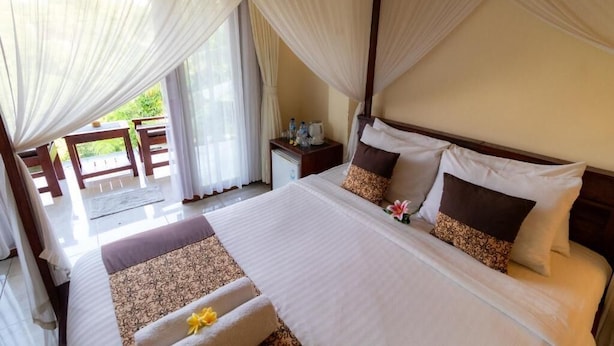 A hotel room with a bed, curtains, a nightstand, and a view of the outdoors. - Room-tranquil Poolside Retreat (Ubud)