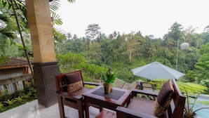 A wooden outdoor seating area with two chairs and a table, overlooking a lush, green landscape with a pool. - Room-tranquil Poolside Retreat (Ubud)