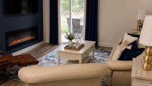 A living room with a flat-screen TV, a fireplace, a ceiling fan, and a sofa. - An Oasis in the Savannah Area (Port Wentworth)