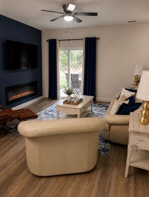 Ein Wohnzimmer mit Flachbildfernseher, Kamin, Deckenventilator und einer Couch.