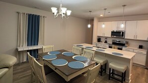 A modern kitchen with white cabinets, a central island, and a dining area with a wooden table and chairs. - An Oasis in the Savannah Area (Port Wentworth)