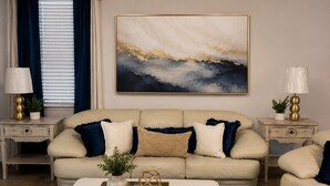 A living room with a beige sofa, two side tables with lamps, a coffee table with decorative items, and a large abstract painting on the wall. - An Oasis in the Savannah Area (Port Wentworth)