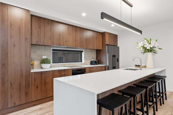 A modern kitchen with wooden cabinets, a large island with bar stools, a built-in oven, and a refrigerator.