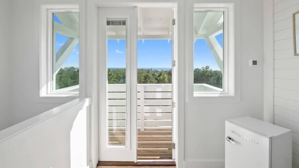 A room with a wooden staircase leading to a balcony with a view of greenery and the sky. - Sleeps 30+ | 30A Estate: Pool, Sauna, Gym, Games! (Santa Rosa Beach)