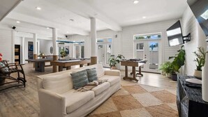 A spacious living area with a sofa, coffee table, and a dining table. There are potted plants and a large window providing natural light. - Sleeps 30+ | 30A Estate: Pool, Sauna, Gym, Games! (Santa Rosa Beach)