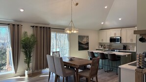 Une cuisine moderne avec des meubles blancs, un îlot central et un coin repas comprenant une table et des chaises en bois.