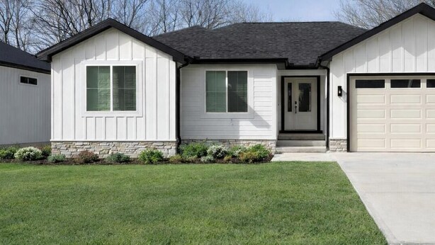 Une maison de plain-pied avec un garage, une porte d’entrée et un petit jardin devant.