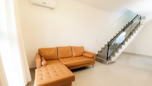 Uma sala de estar moderna com um sofá de couro, uma escada de vidro e piso revestido de azulejos.