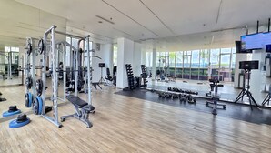 A modern gym with various weightlifting equipment, large windows, and a spacious layout. - TenLira By SanLiving - 1BR - PIK (Jakarta)