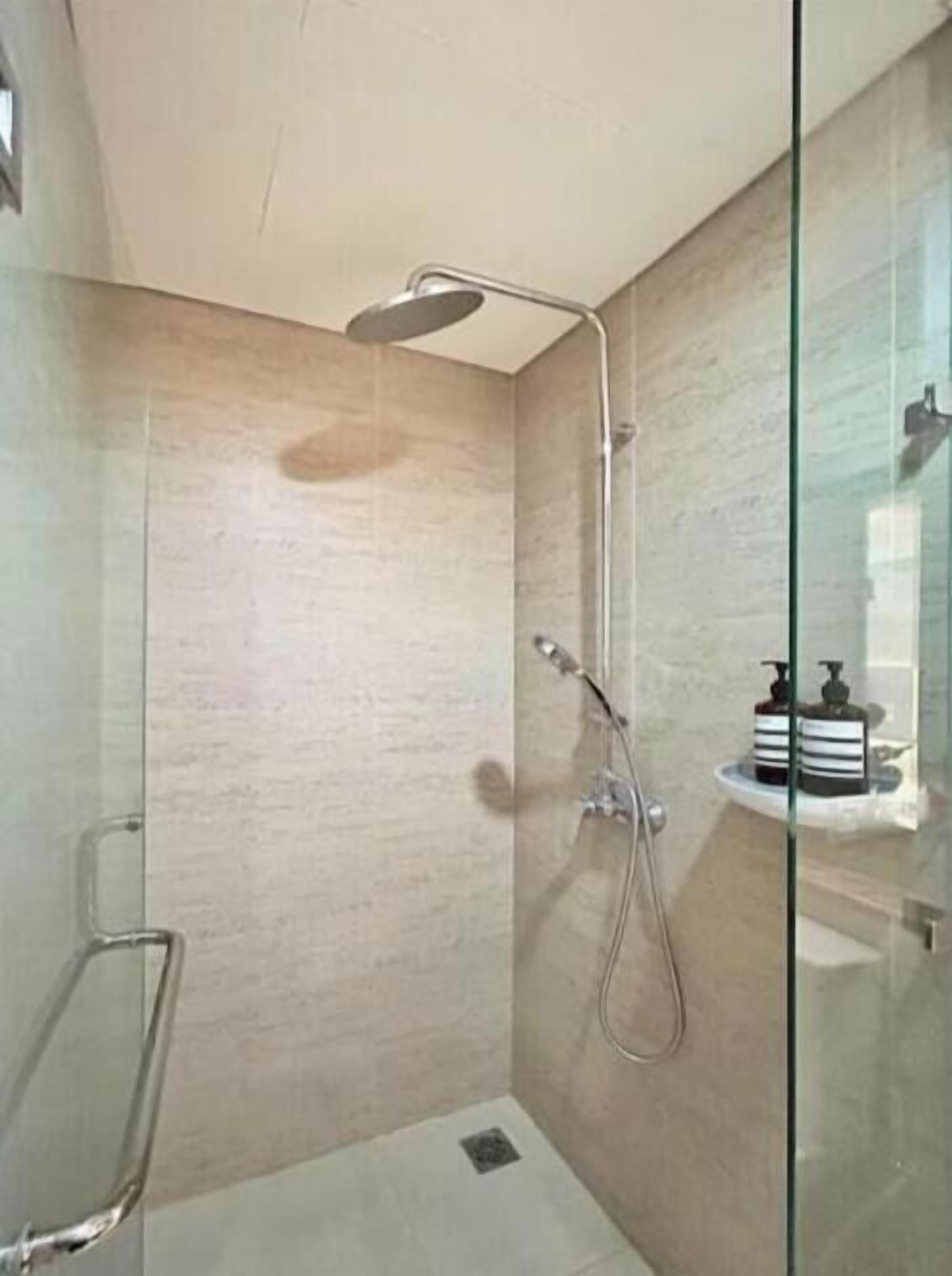 A modern bathroom with a glass shower enclosure, a handheld showerhead, and a wall-mounted faucet.