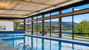 An indoor swimming pool with a view of mountains and a lake.