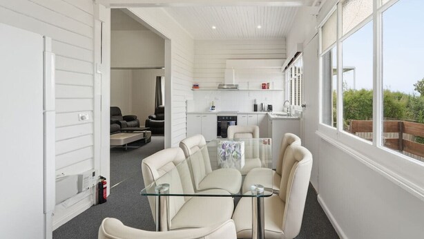 Een moderne keuken met witte kastjes, een eethoek met een glazen tafel en stoelen, en uitzicht op groen.