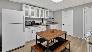 Cozinha moderna com armários brancos, micro-ondas, cafeteira e mesa de madeira com bancos.