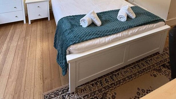 Een keurig opgemaakt slaapkamer met een bed, twee nachtkastjes met lampen, een kledingkast en een kamerkleed met dessin.
