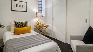 Une chambre d’hôtel avec un lit, une table de chevet avec une lampe, une chaise, une fenêtre et une porte.