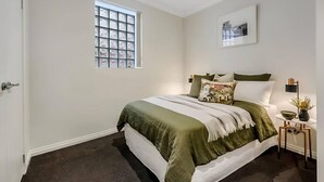 Une chambre à coucher avec un lit, une fenêtre, une table de chevet et un tableau accroché au mur.