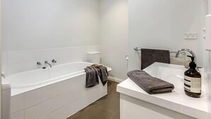 Une salle de bain moderne avec une baignoire blanche, un lavabo blanc et un grand miroir.