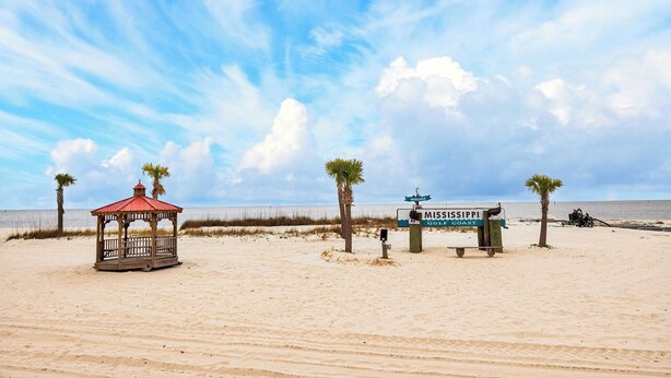 Une plage avec un kiosque, des palmiers et un panneau indiquant la région du golfe du Mississippi.