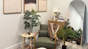 Un salon moderne avec un fauteuil vert, une petite table ronde, une plante en pot, un miroir et des œuvres d’art abstraites accrochées au mur.