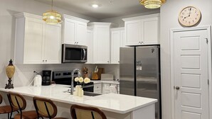 Une cuisine moderne avec des meubles blancs, un îlot central doté de tabourets, des appareils en acier inoxydable et un éclairage décoratif.