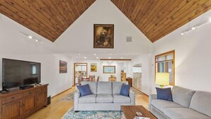 Un salon spacieux avec un plafond haut, un grand téléviseur à écran plat, un canapé gris et un meuble en bois.