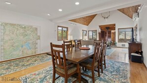 Un vaste espace dédié à la salle à manger, avec une grande table et des chaises en bois, une carte accrochée au mur et un plafond haut avec des poutres apparentes.