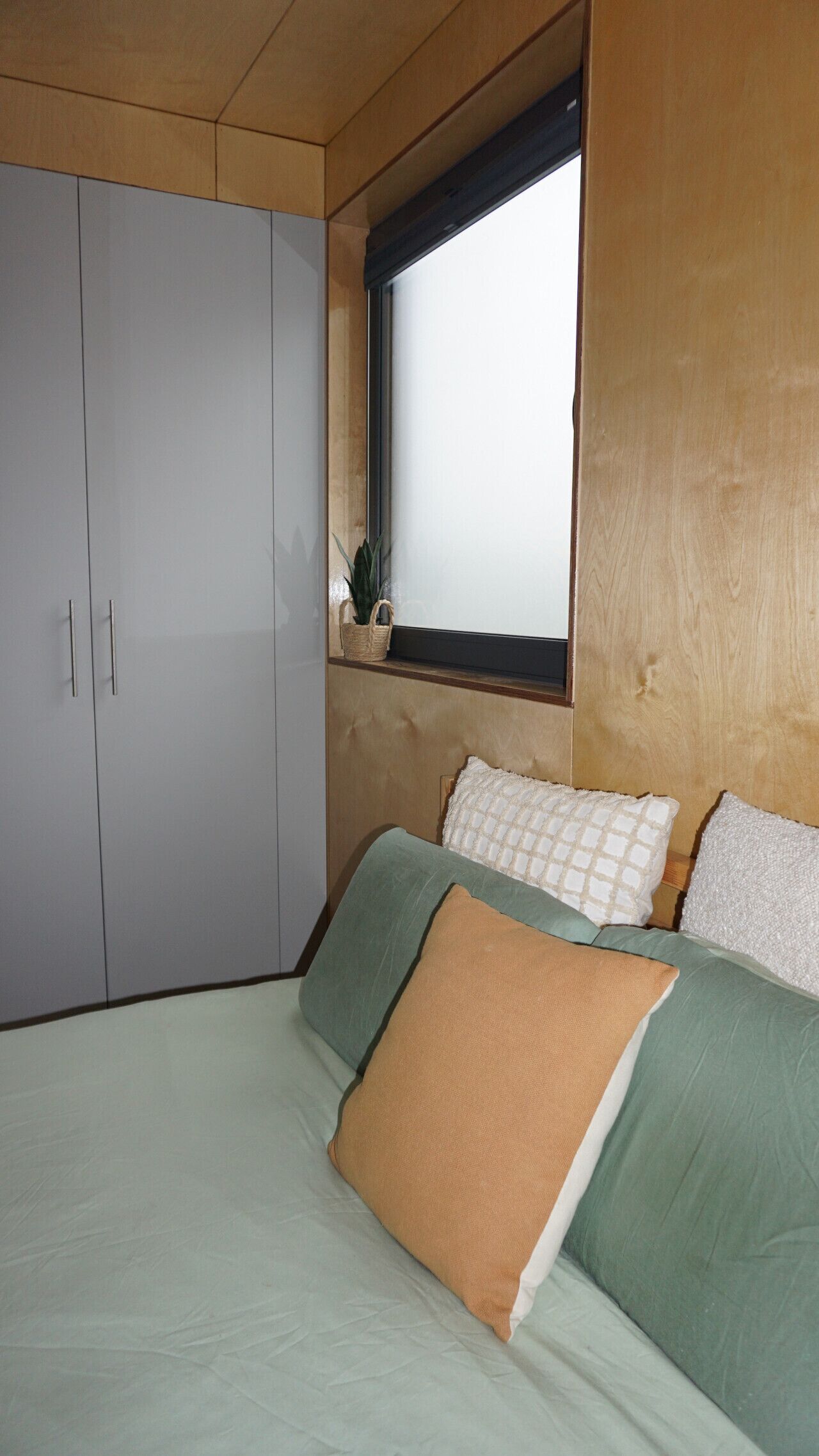 A bedroom with a bed, pillows, a window, and a wardrobe.