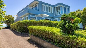 Een gebouw met twee verdiepingen, een blauwe gevel, een overdekt terras en goed onderhouden hagen.