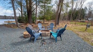 A gravel patio with Adirondack chairs and a fire pit. - Lakefront Poconos 5BR | Hot Tub • Dock • Near Ski (Blakeslee)
