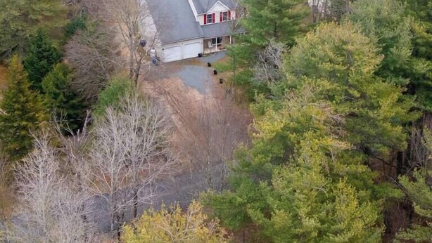 A house with a garage, surrounded by dense trees and a lake. - Lakefront Poconos 5BR | Hot Tub • Dock • Near Ski (Blakeslee)