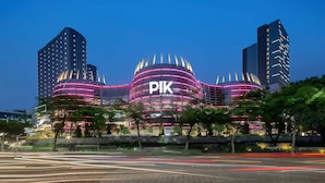 Um edifício moderno com uma placa grande 'PIK', rodeado por árvores e outras construções.