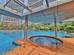 Ein moderner Hotelpoolbereich mit Whirlpool, Holzterrasse und Blick auf hohe Gebäude.