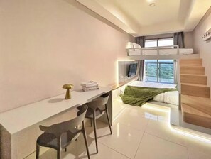 Een moderne hotelkamer met een stapelbed, een bureau met stoelen, een kleine tafel met een lamp, en een trap naar een hoger niveau.