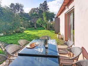 Un patio con una mesa de vidrio, sillas de mimbre y vistas a un jardín exuberante y árboles.