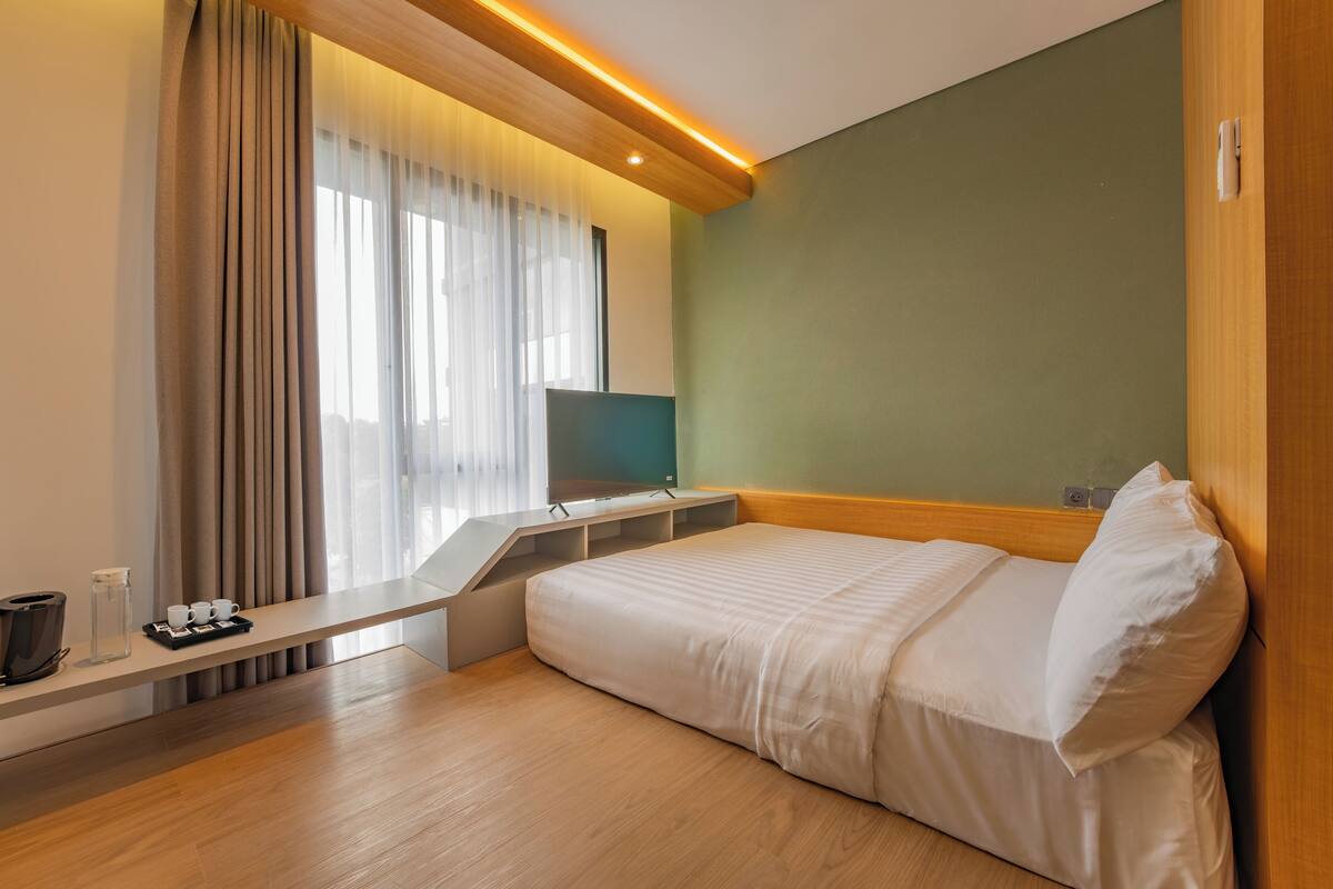 A modern hotel room with a bed, a desk, a chair, a TV, and a window with curtains.