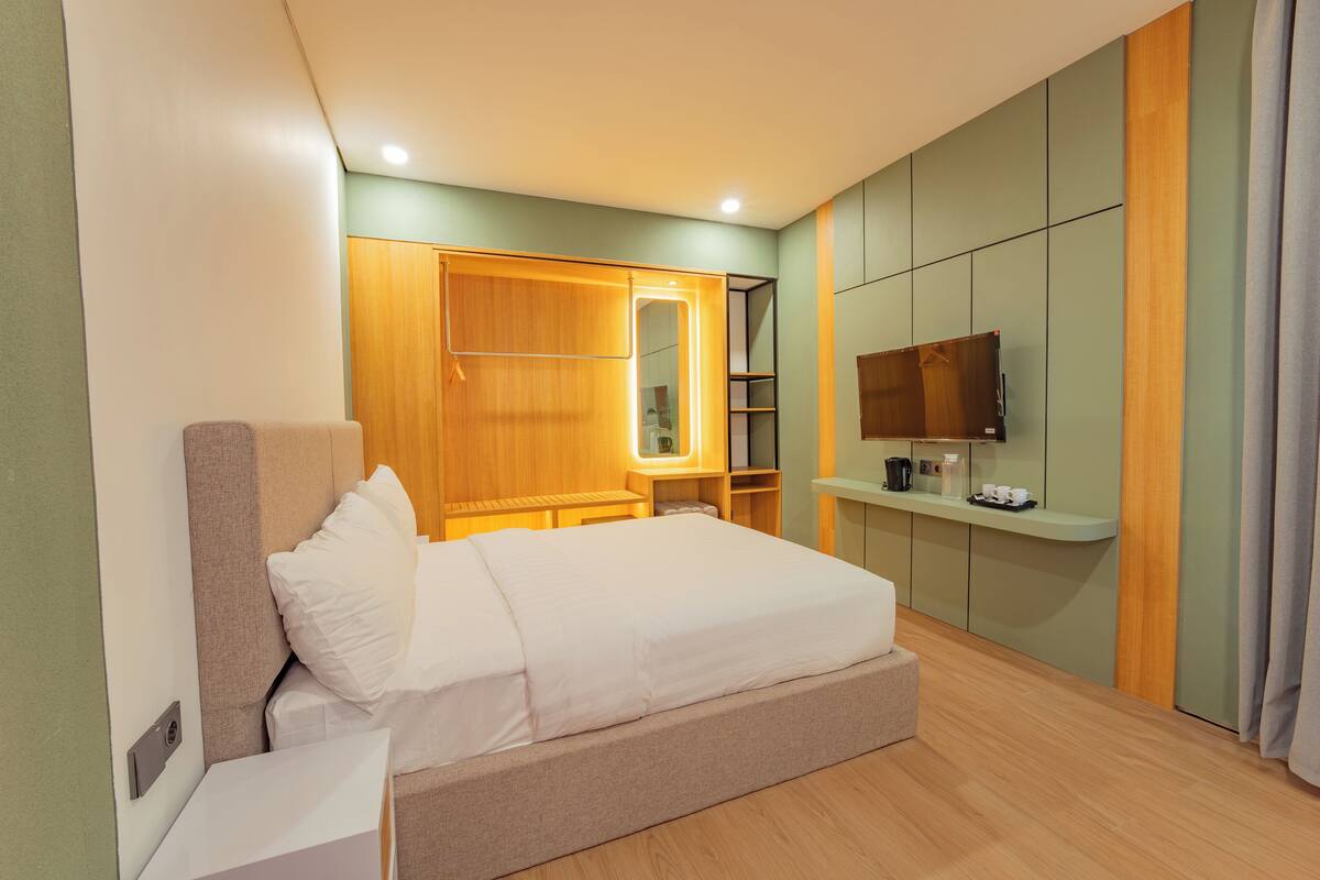 A modern hotel room with a bed, bedside table, wardrobe, and built-in TV.
