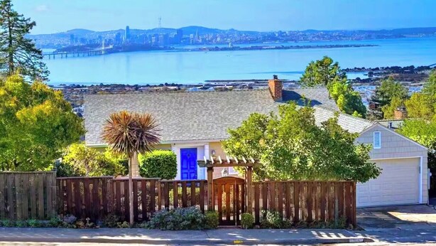 A residential area with a blue door, a wooden fence, and a view of a bridge and water body in the distance.