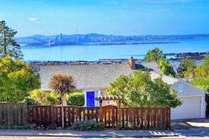 Un quartier résidentiel avec une porte bleue, une clôture en bois et, au loin, une vue sur un pont et une étendue d’eau.