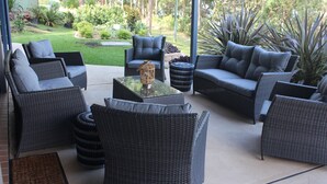 Un espace extérieur aménagé, abrité et doté de mobilier en osier et d’une table basse en verre.