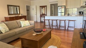Un salon moderne comprenant un canapé, une table basse et un coin cuisine avec un réfrigérateur et des tabourets de bar.