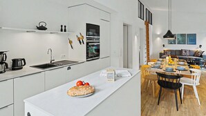 Een moderne keuken met een centraal eiland, een eetgedeelte met een houten tafel en stoelen, en een woongedeelte met een bank en wanddecoratie.
