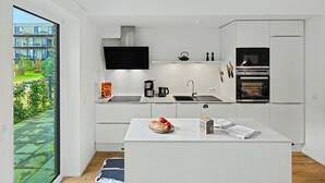 Een moderne keuken met een centraal eiland, inbouwapparatuur en uitzicht op een woongebouw.