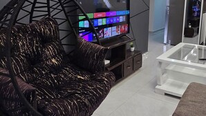 Ett modernt vardagsrum med en hängstol, en platt-TV och ett soffbord i glas.