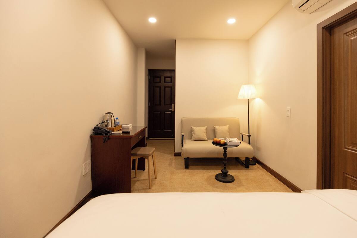 Habitació d'hotel amb un llit, una taula de treball amb una làmpada, una cadira i un sofà.