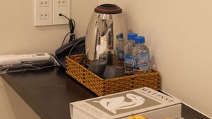 Un comptoir dans une chambre d’hôtel avec une machine à café, des bouteilles d’eau, un livre et des pommes.